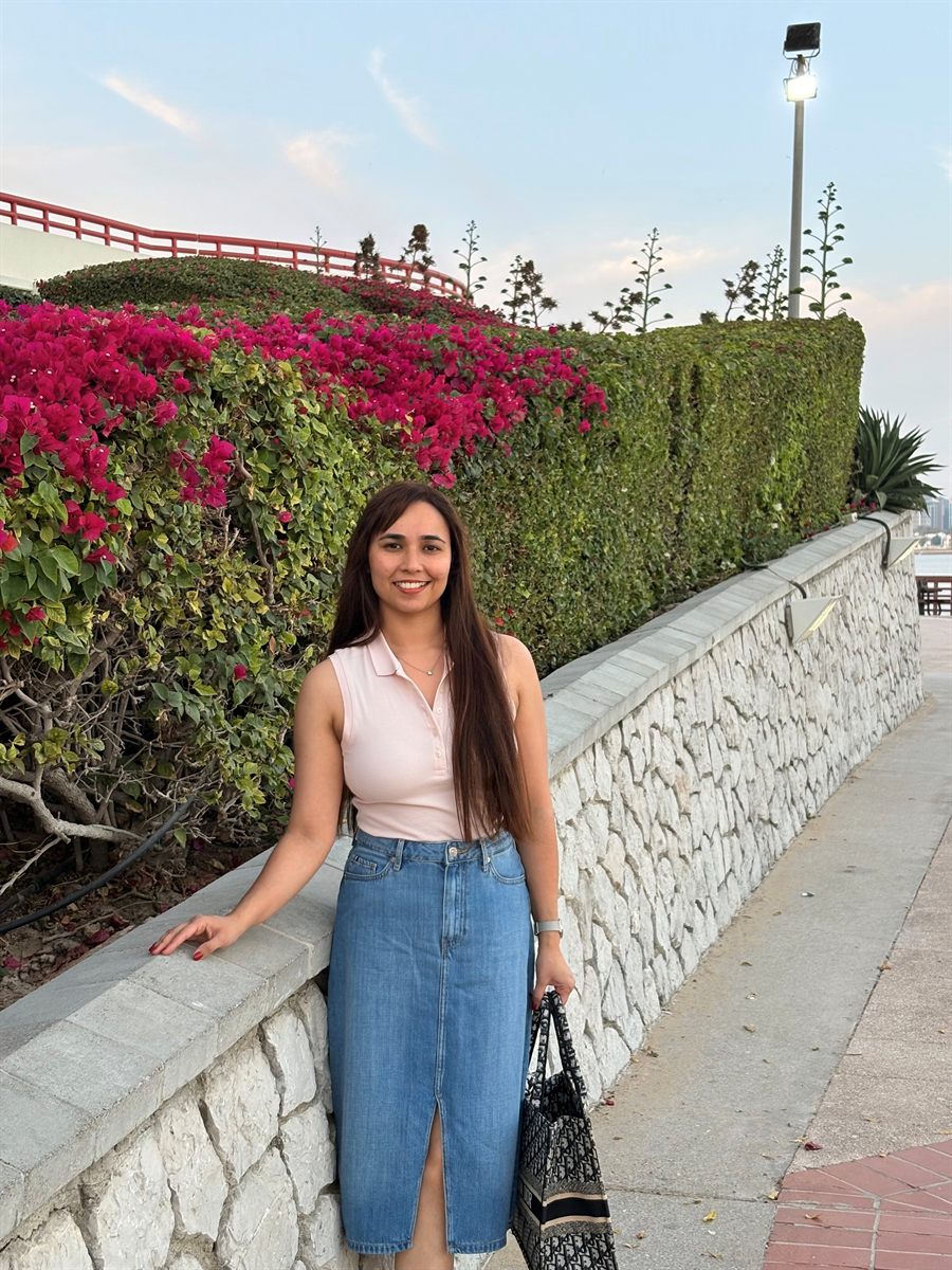 Astha Machra smiling beside a stone wall covered in pink bougainvillea